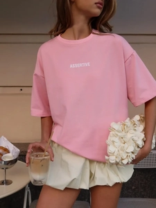 Dettaglio di una maglietta rosa in cotone con stampa e borsa con fiori 3D all'aperto