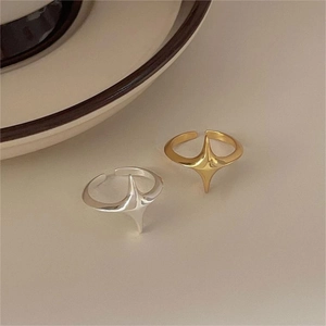 Close-up of minimalist gold and silver four-pointed star rings on a cream background