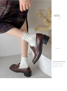 Close-up of brown vintage loafers with white ruffle socks and dark plaid skirt styling