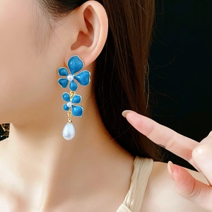Detail of vintage blue enamel flower earrings with pearls worn by a model on black background