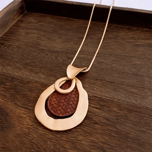 Detail of vintage matte gold teardrop pendant with woven wood texture on wood tray
