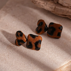Macro detail of heart and square leopard print earrings on a textured stone base