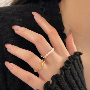Close-up of golden wave texture ring and white pearl ring set on a model's hand