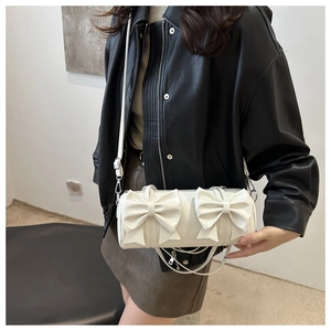 Detailed view of white cylinder bag with double bow decoration and slim shoulder strap