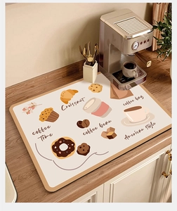 Detail of absorbent coffee machine mat with croissant illustrations on wooden counter