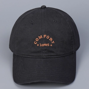 Close-up of orange COMFORT ZONES embroidery on a premium black cotton baseball cap