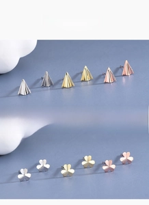 Detailed view of silver and gold paper plane and clover stud earrings in three finishes