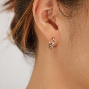 Macro detail of silver geometric hoop earrings with diamond-cut texture and shimmering finish