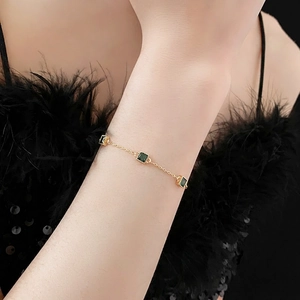 Elegant gold plated bracelet with square green zircons shown on a model's wrist