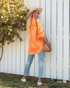 Detail view of orange denim jacket featuring distressed back holes and frayed hem finish