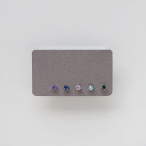 Macro detail of five pairs of assorted colorful gemstone stud earrings on a display card