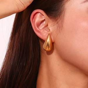 Detail of gold teardrop earring with ribbed texture worn by a model in close-up view