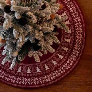 Mini red knit Christmas tree skirt with white snowflake patterns on a wood surface