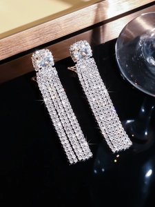 Close-up of sparkling long tassel earrings with pave zircon crystals on black surface