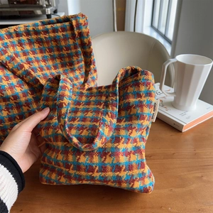 Detail of two knitted houndstooth tote bags in red and orange on a wooden table