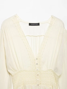 Macro view of the delicate lace trim and round white buttons on the beige V-neck blouse