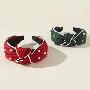 Close-up of red and green knotted headbands with white pearls and satin texture