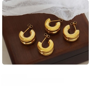 Detail of gold double C-shaped earrings on wood texture with soft fabric accents