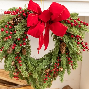 Detail of heart-shaped Christmas wreath with red berries, pine needles and a velvet bow