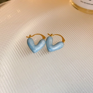 Macro shot of sky blue heart-shaped earrings with golden edges on a textured tray