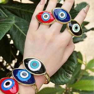 Close-up of vibrant retro evil eye enamel bracelets and rings worn on a hand outdoors.