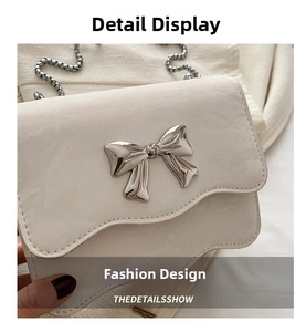Detail of white wave-edge crossbody bag with a large silver metal bow and chain strap