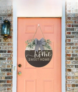 Detail of wooden Home Sweet Home sign with striped bow and eucalyptus on orange door