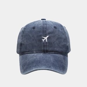 Detailed view of white airplane embroidery on washed blue denim baseball cap cotton fabric