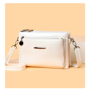 Close-up of white PU leather crossbody bag featuring double zippers and a metal charm