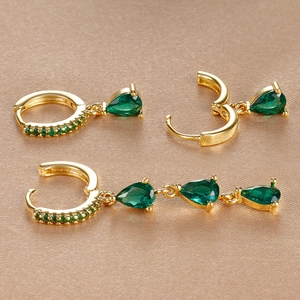 Macro view of three-piece gold drop earrings with emerald zircon on champagne silk fabric