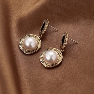 Détail de boucles d'oreilles perles vintage avec cadre doré sur fond de soie marron