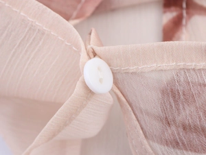Detail of light pink chiffon fabric with fine pleats and a white round button fastening