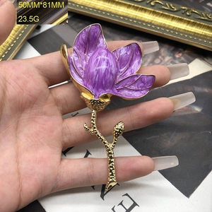 Detailed shot of purple enamel magnolia brooch with gold stem held by hand, 50mm x 81mm