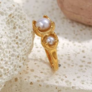 Dettaglio macro dell'anello dorato 18K con due perle bianche su una pietra corallo