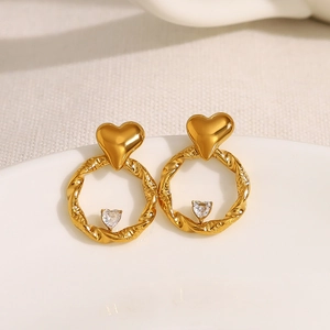 Golden heart earrings with twisted texture and centered zircon on a white ceramic tray