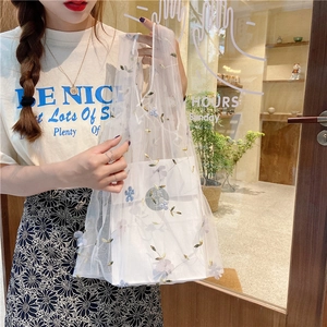 Detail of white mesh tote bag with floral embroidery and gift box inside handled by model