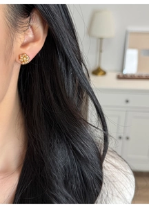 Close-up of golden hydrangea floral stud earrings worn by a model in soft indoor lighting