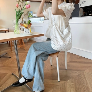 Detail of a large white polka dot canvas tote bag with a long shoulder strap
