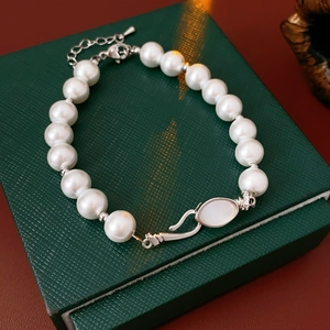 Close-up of pearl bracelet with shell inlay on green jewelry box and red table