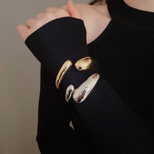 Macro view of fluid organic teardrop bangles in polished gold and silver finishes