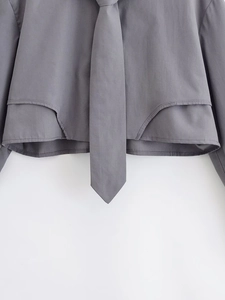 Detail of grey cropped shirt featuring asymmetric curved hem and matching necktie