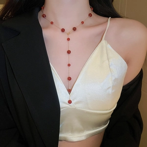 Detail of a red beaded Y-shaped gold-plated necklace worn by a female model