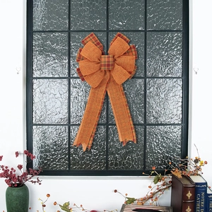 Detail of orange burlap Thanksgiving bow with plaid edges on a glass window background