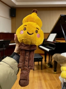 Detail of yellow cartoon musical instrument plush toy with embroidery held in hands