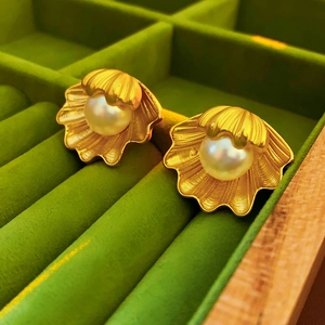 Close-up of vintage golden shell earrings with white pearls on green velvet