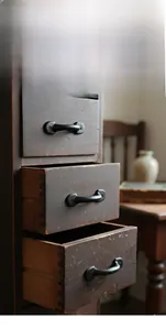 Detail of vintage cast iron handle on dark wood drawer showing rustic texture