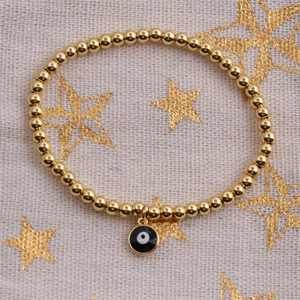 Detailed close-up of gold-plated evil eye beaded bracelet on starry textured fabric