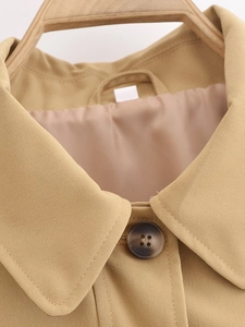 Détail du col et du bouton du trench-coat montrant la texture du tissu en sergé de coton