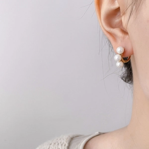 Detailed close-up of gold pearl hoop earrings with three pearls on a female model