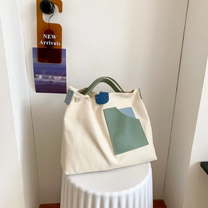 Detail of canvas tote bag with green handles and colorful faux leather front pockets